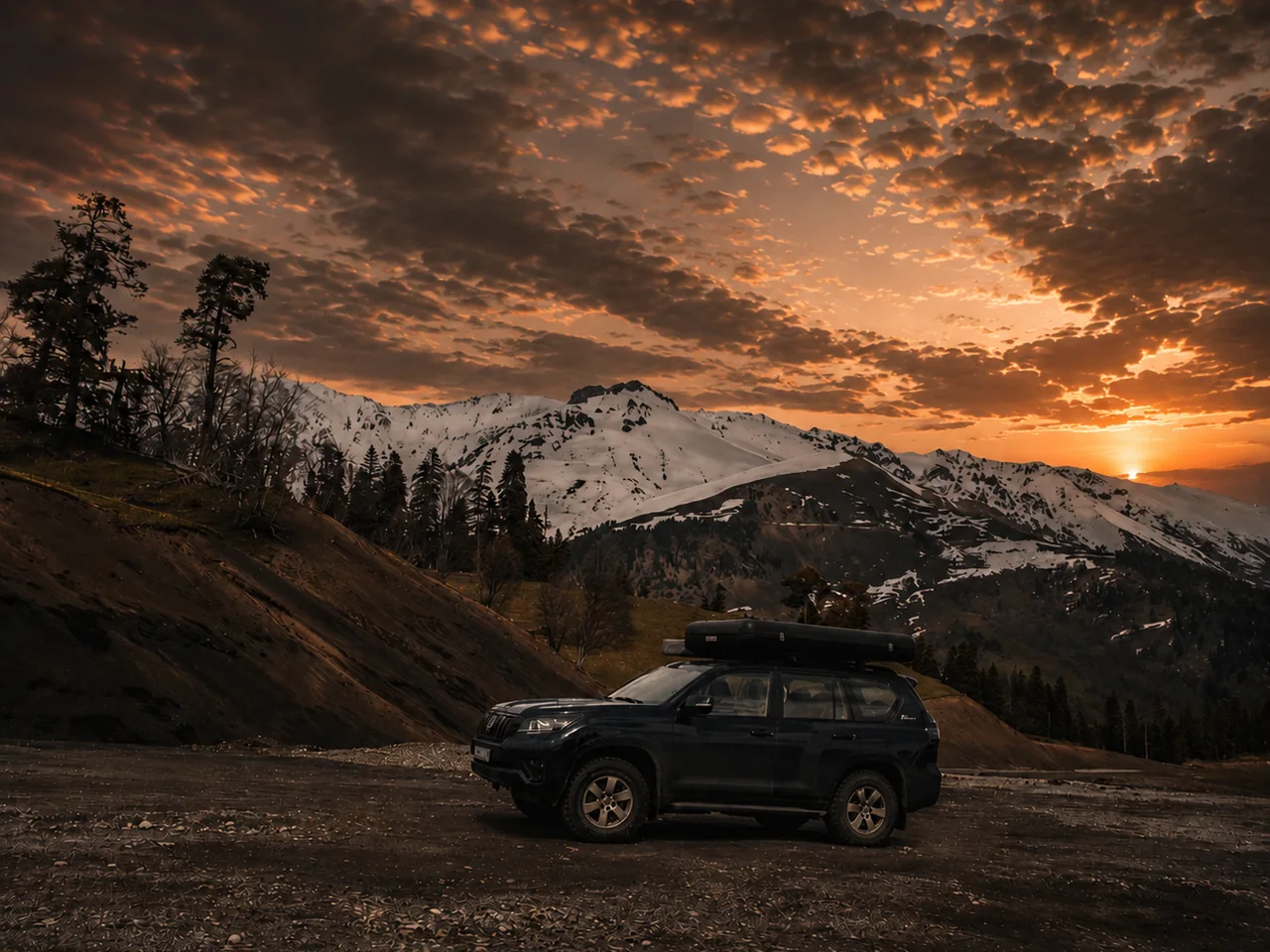 Toyota Land Cruiser Prado с боксом на крыше на смотровой площадке в горах на закате